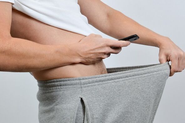 muž se dívá přes kalhoty na zvětšený penis